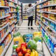 Bulk grocery shopping essentials including rice bags, noodles, cooking oil, beans, tinned foods, and snacks arranged on a kitchen counter
