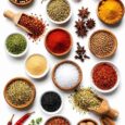 A colourful selection of essential kitchen spices including curry powder, paprika, turmeric, garlic powder, thyme, black pepper, cinnamon, nutmeg, ginger, and cayenne pepper arranged in bowls with fresh herbs, showcasing pantry staples for everyday cooking.